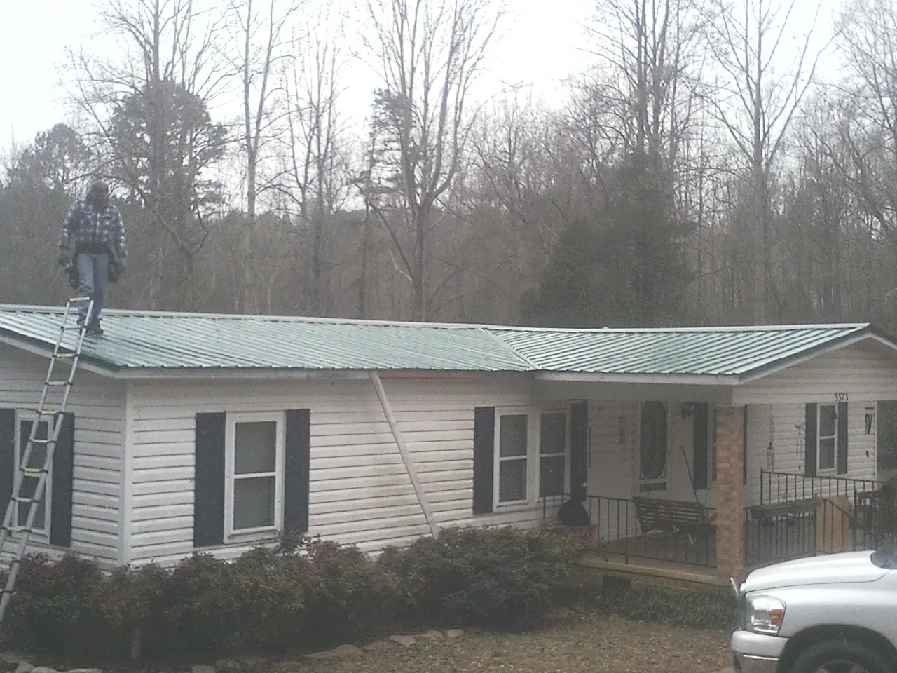 Worker on a ladder beside a new green metal roof on a ranch home in Hamlin