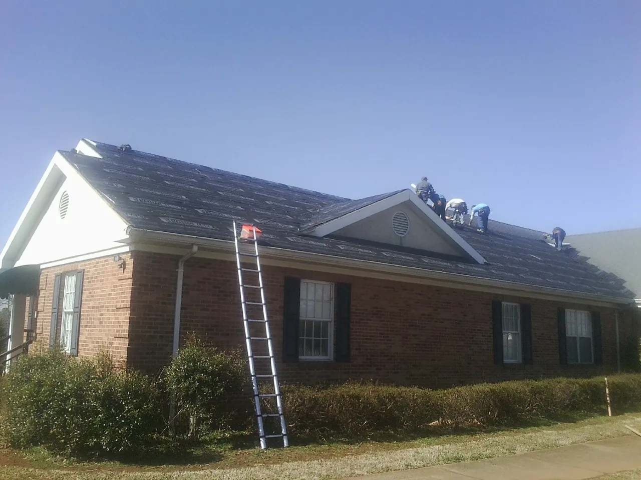 Crew tearing shingles off a brick ranch roof with a ladder set — Emergency Roof Repair work by our crew in Hamlin