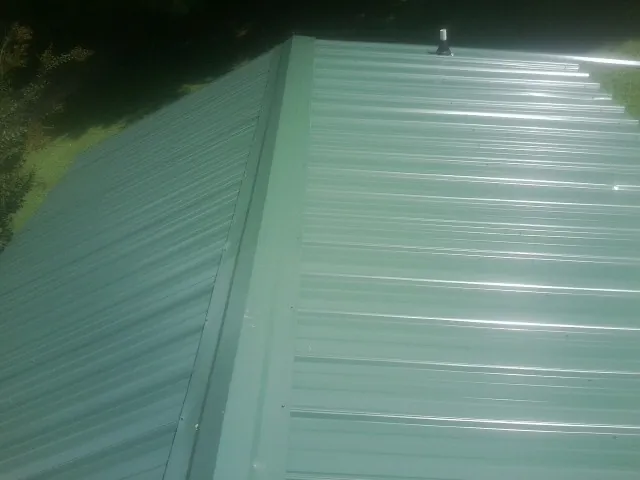 New green metal panels meeting at the ridge of a roof — Flat Roof Repair work by our crew in Hamlin